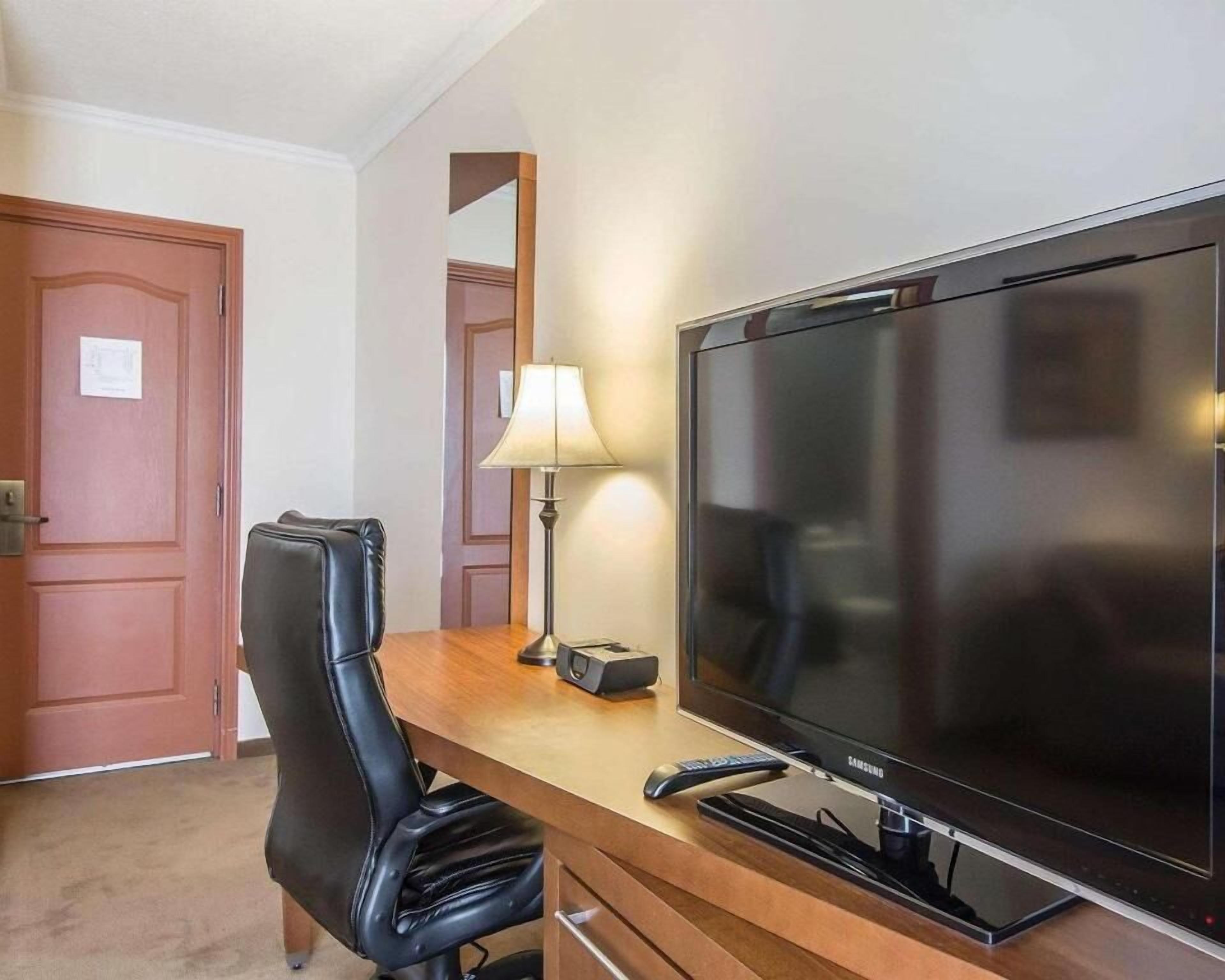 Une chambre d’hôtel dotée d’un grand téléviseur à écran plat, d’un fauteuil en cuir, d’un bureau avec une lampe et de portes en bois.