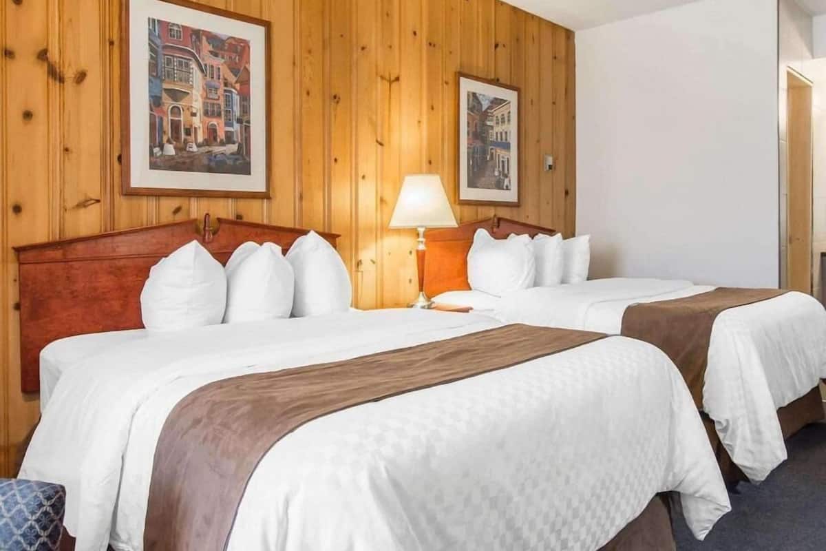 A hotel room with two beds, wooden paneling on the walls, and framed pictures.