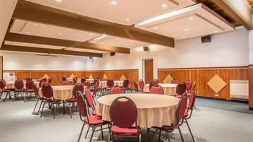 A conference room with round tables and red chairs, wooden paneling on the walls, and recessed ceiling lighting.