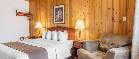 Quarto com painéis de madeira, uma cama, duas luminárias de apoio, uma cadeira e um quadro emoldurado na parede.