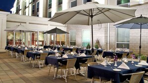 An outdoor dining area with tables set for a meal, umbrellas, and a building in the background.