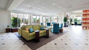 A spacious lobby with a green sofa, blue armchairs, and a coffee table. Large windows provide natural light and views of the outdoors.