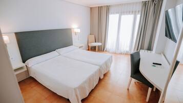 Habitación de hotel con dos camas, un escritorio, una silla, un televisor y una ventana con cortinas.