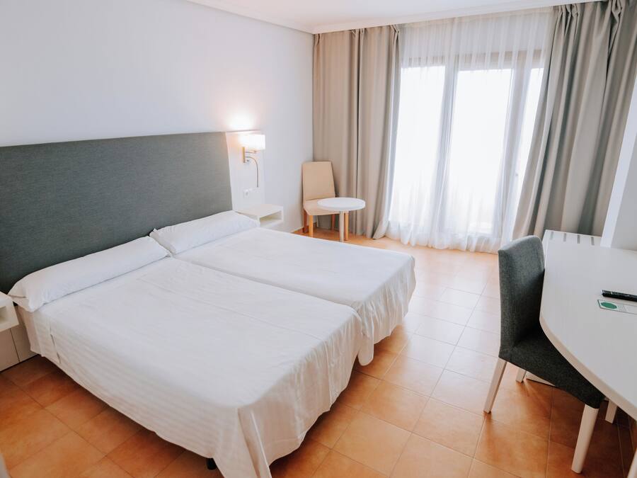 Habitación de hotel con dos camas, un escritorio, una silla, un televisor y una ventana con cortinas.