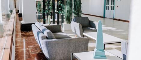 A modern lobby with grey sofas, a white table, and a tall blue sculpture.