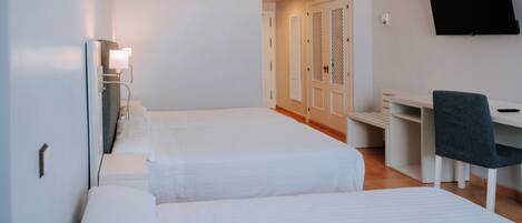Quarto de hotel com duas camas, uma escrivaninha, uma cadeira e uma televisão na parede.
