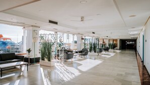 A spacious lobby with a high ceiling, large windows, and a view of the cityscape. There are several seating areas with tables and chairs, and potted plants are placed throughout the space. - Hotel Bahía Sur (San Fernando)