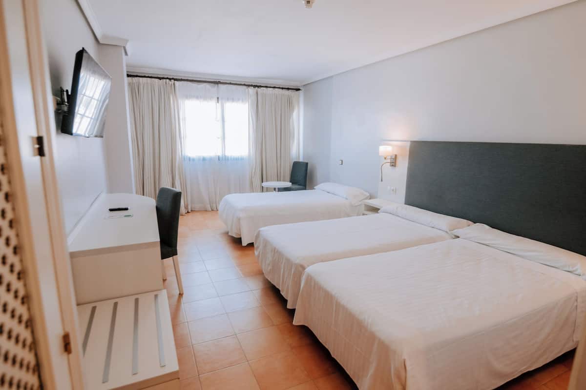 A hotel room with two beds, a desk, a chair, and a TV mounted on the wall.