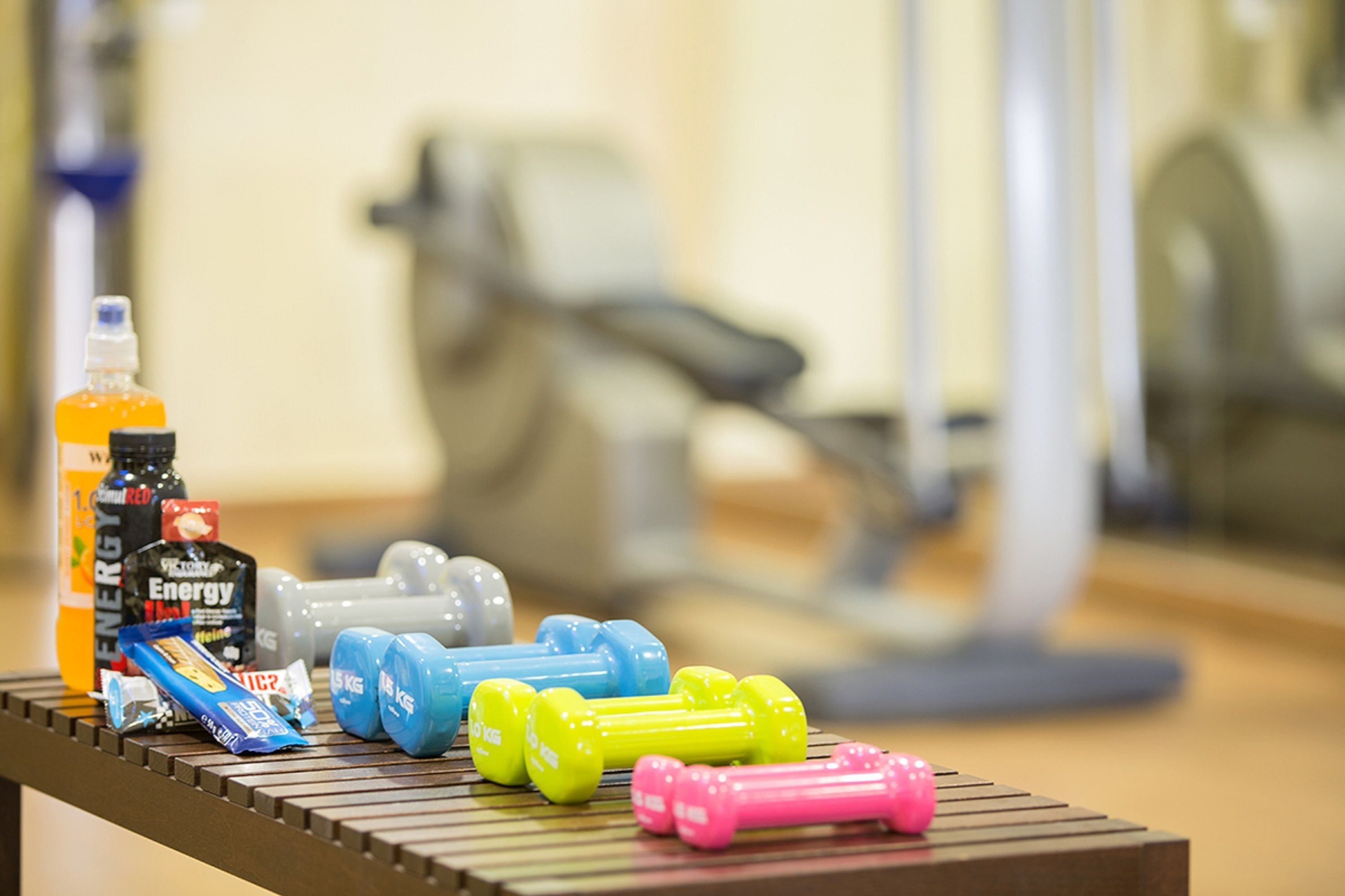 A gym with exercise equipment and energy drinks on a bench.