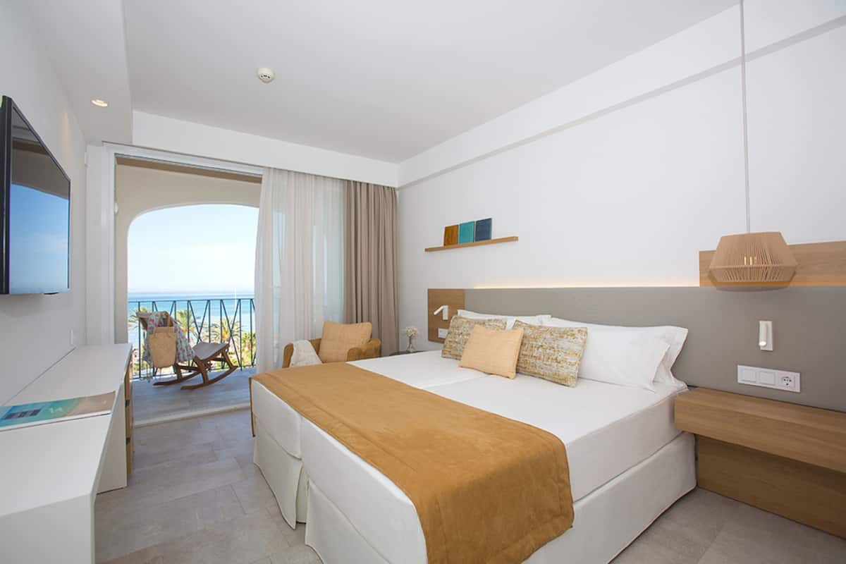 A modern hotel room with a large bed, a desk, and a balcony with a view.