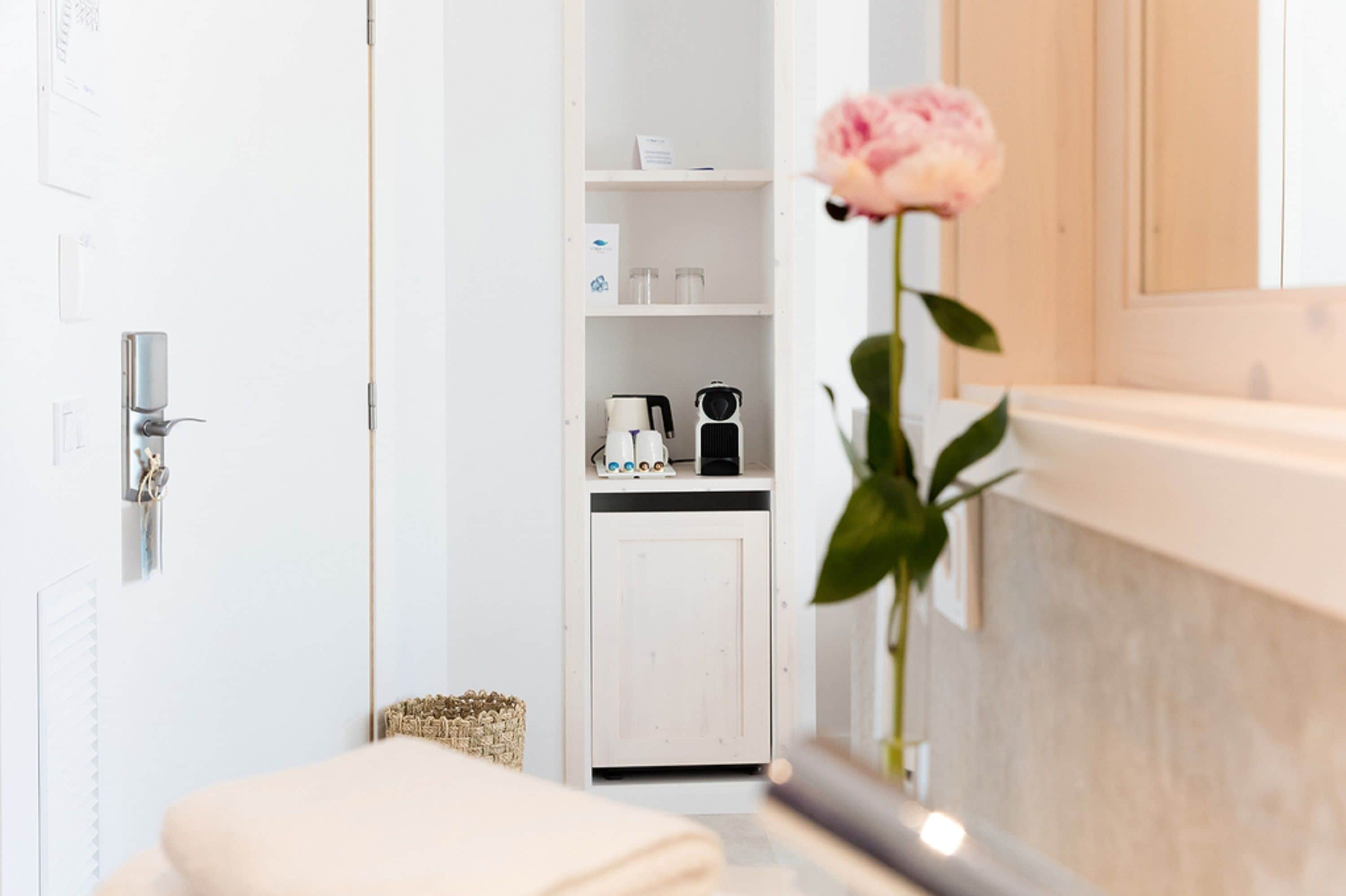 Un baño con lavamanos blanco, un espejo y una rosa en un florero.