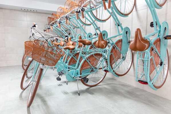 A row of turquoise bicycles with brown leather seats and wicker baskets, arranged in a modern indoor setting with tiled walls and a concrete floor.