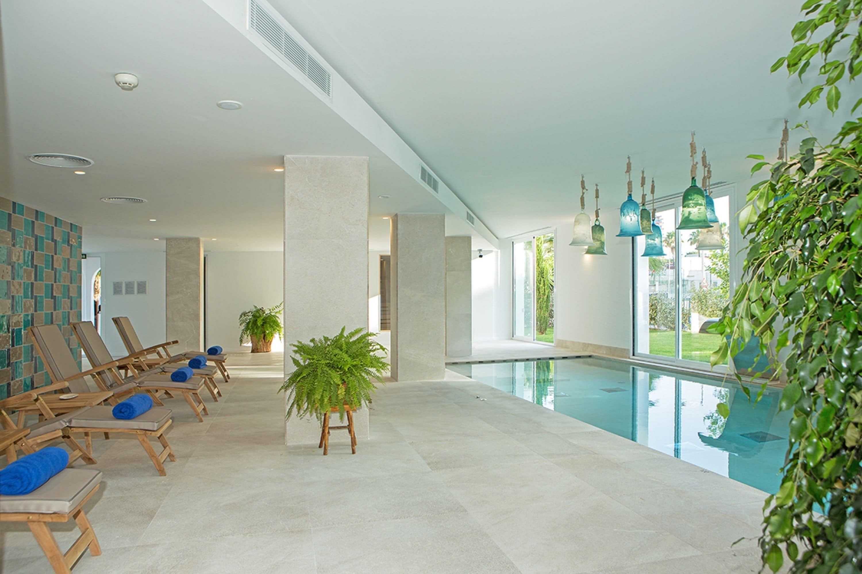 Un área moderna de piscina interior con sillones de descanso y una planta en maceta.