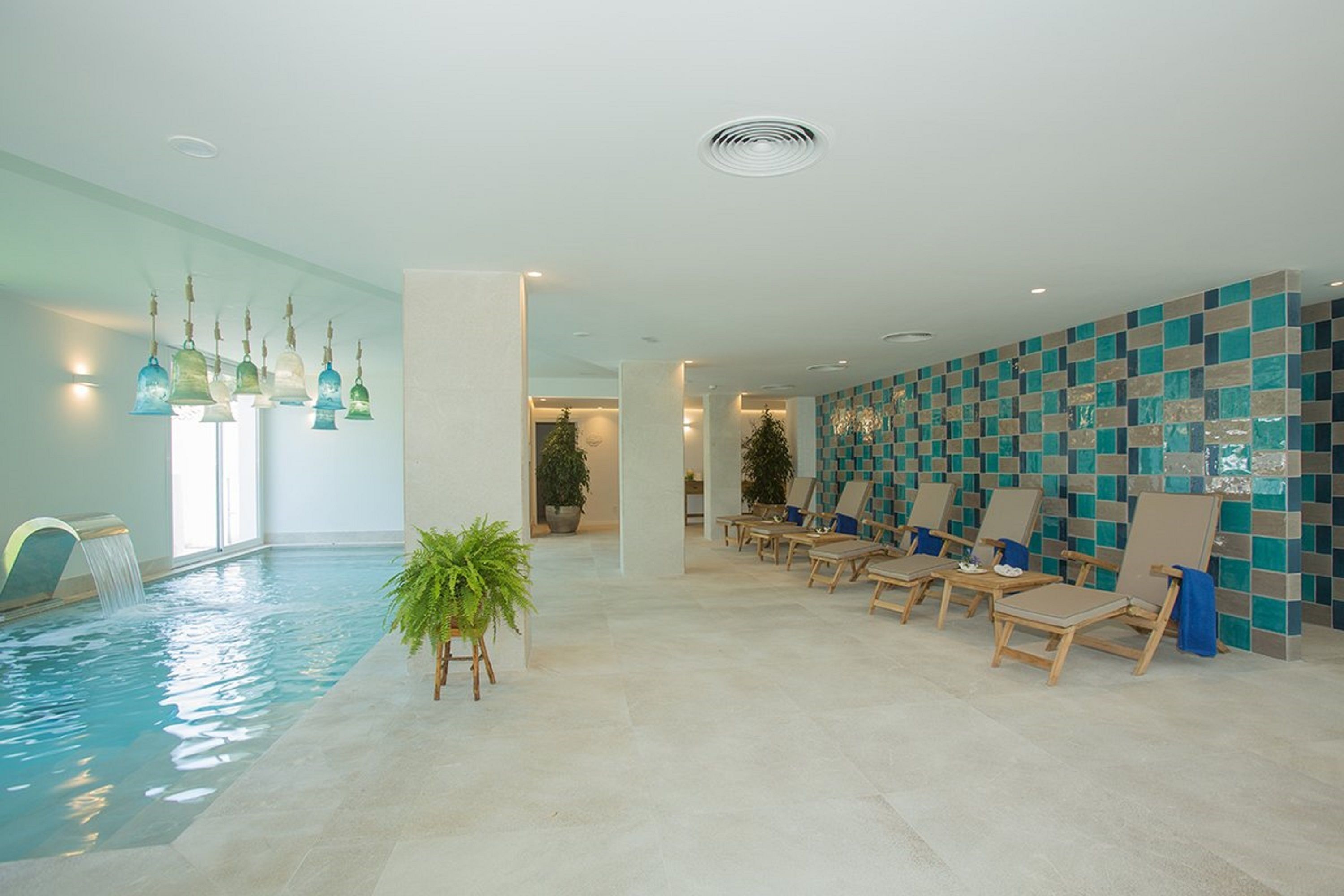 An indoor swimming pool with lounge chairs and a tiled wall.