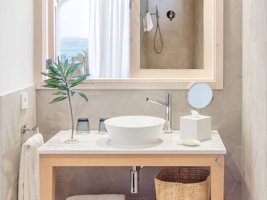 A bathroom with a large mirror, a round sink, a towel rack, and a small plant.