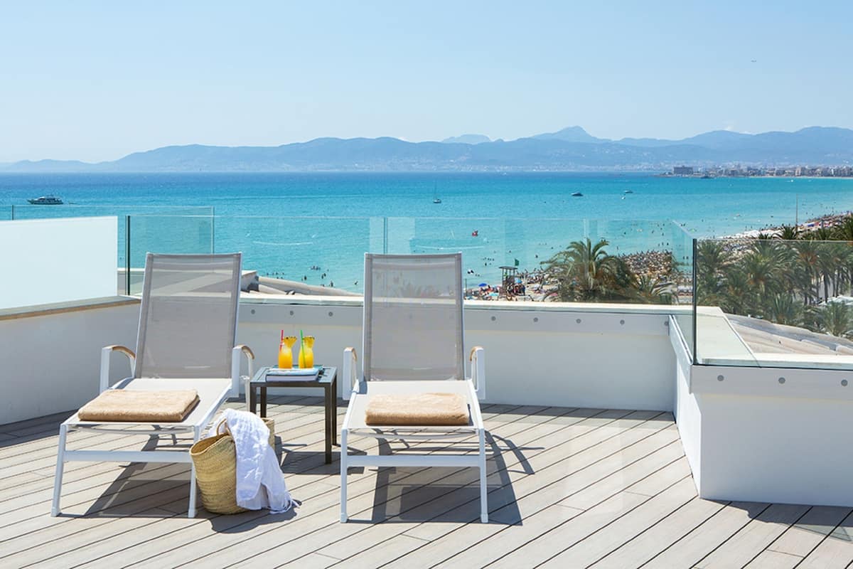 A balcony with two sun loungers, a small table with drinks, and a beach view.