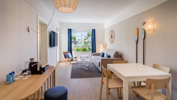 A modern hotel room with a dining area, a sofa, a TV, and a view of the outdoors.