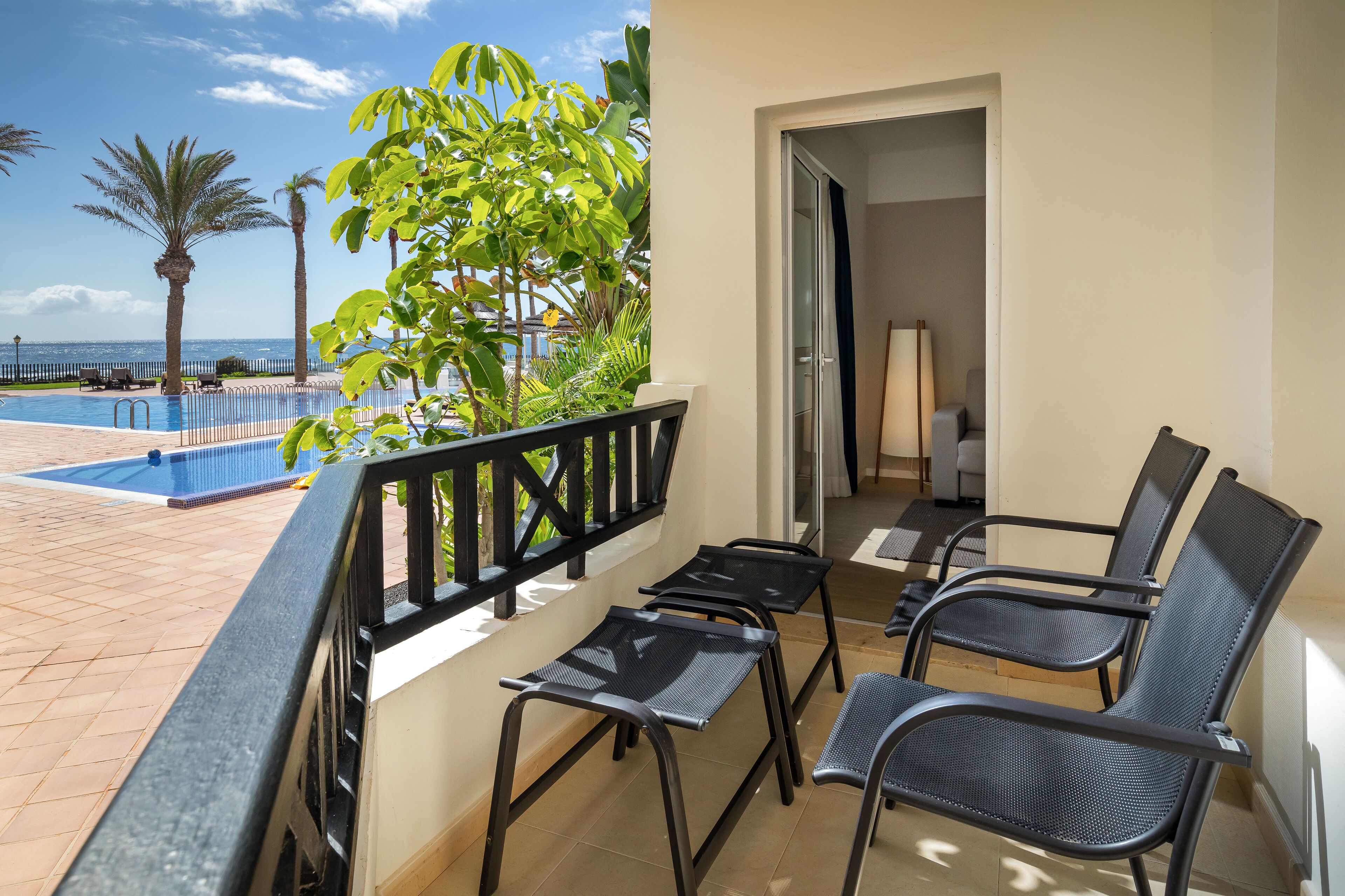 A balcony with a pool view, black metal chairs, and a door leading to a room.