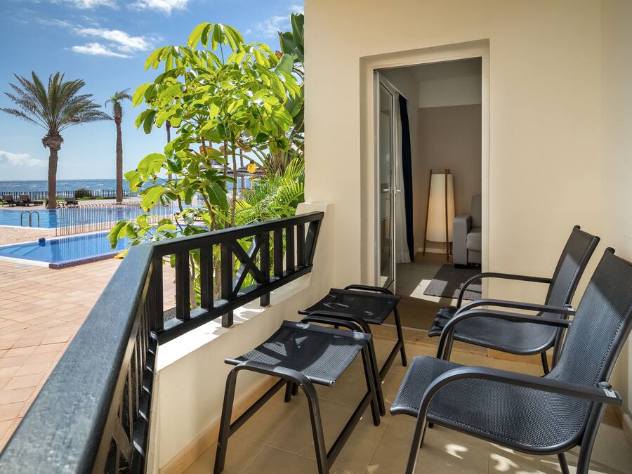 A balcony with a pool view, black metal chairs, and a door leading to a room.