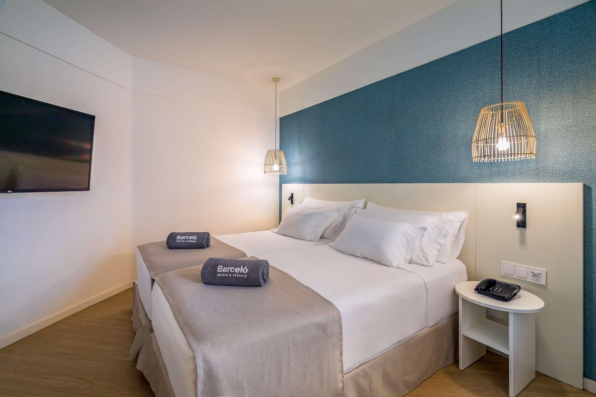 Ein Hotelzimmer mit einem großen Bett, zwei Nachttischen, einem Flachbildfernseher und einer blauen Akzentwand.