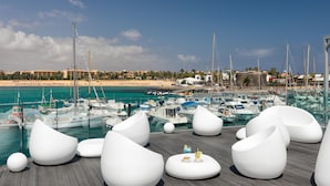 Marina con barcos amarrados, playa al fondo y zonas de estar blancas y modernas.