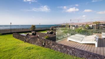 A coastal outdoor area with a stone wall, lounge chairs, and a glass railing overlooking the sea.
