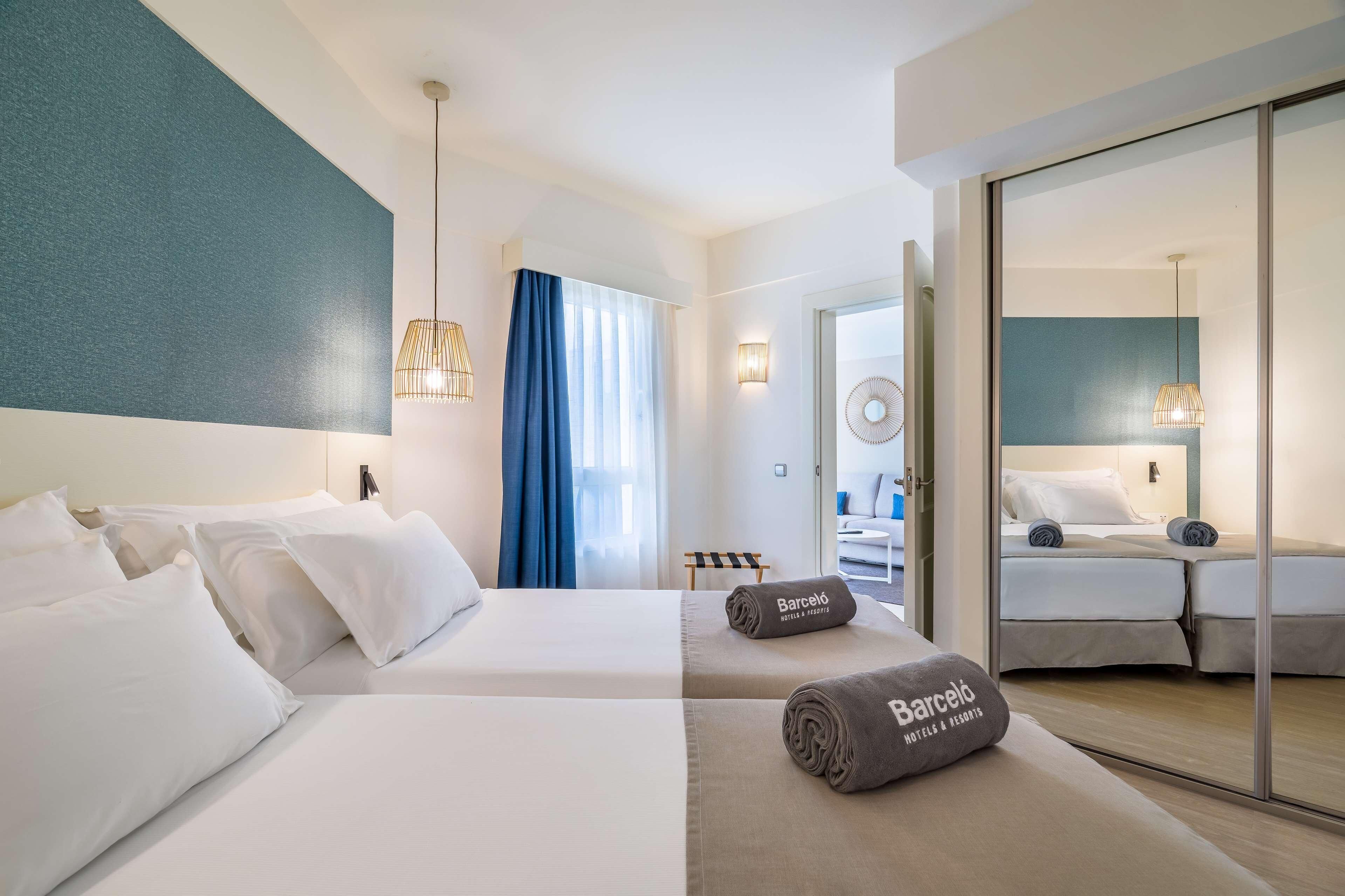 A hotel room with two beds, a large mirror, a minibar, and a view of the city.