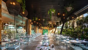 Un área de comedor al aire libre con mesas y sillas, cestas colgantes con plantas y vistas al follaje circundante.