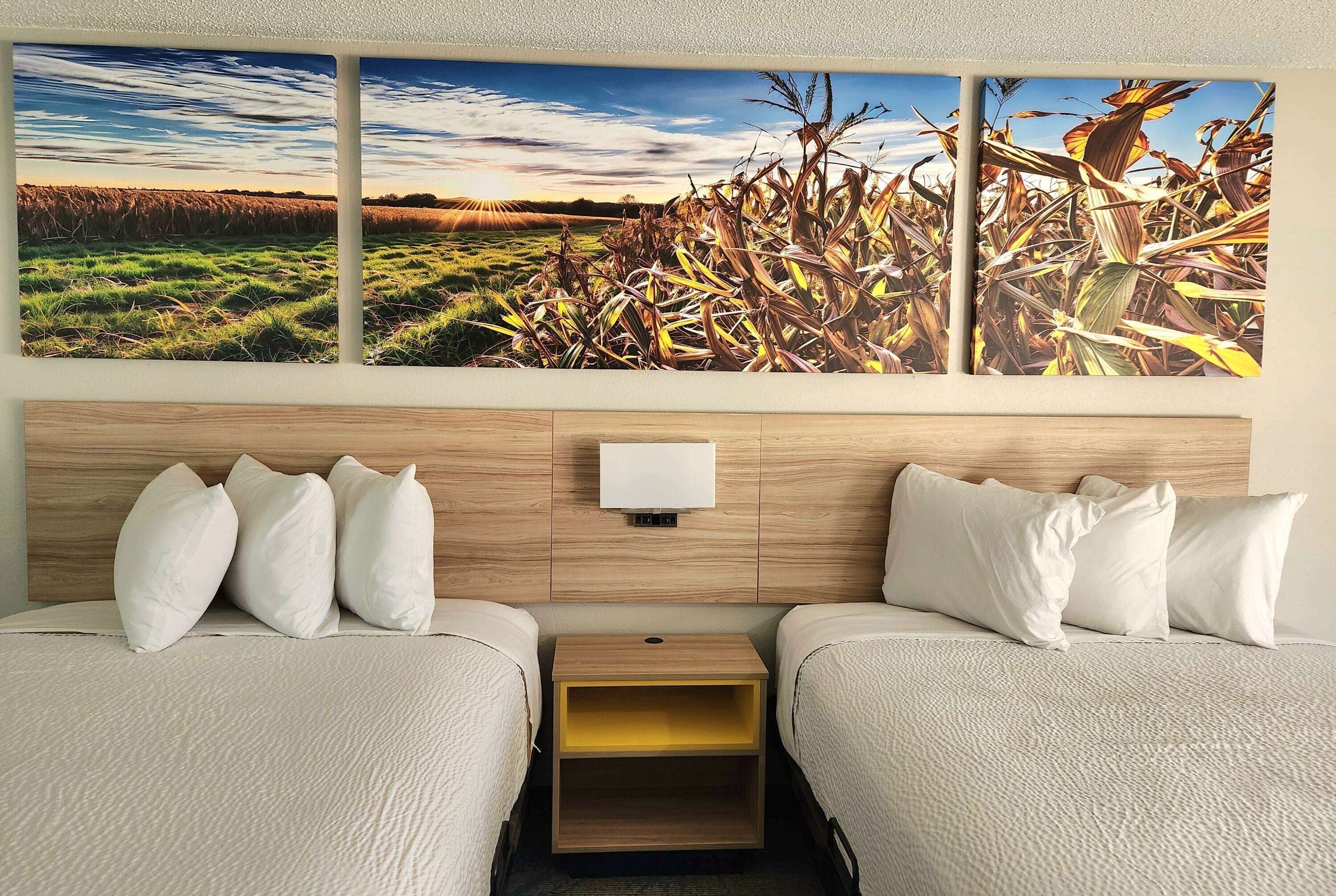 A hotel room with two beds, a wooden headboard, a nightstand, and a wall-mounted lamp.