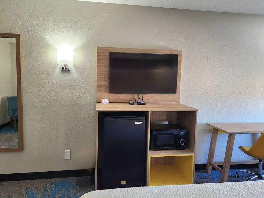 Habitación de hotel con cama, escritorio con silla, televisor montado en la pared, microondas y refrigerador.
