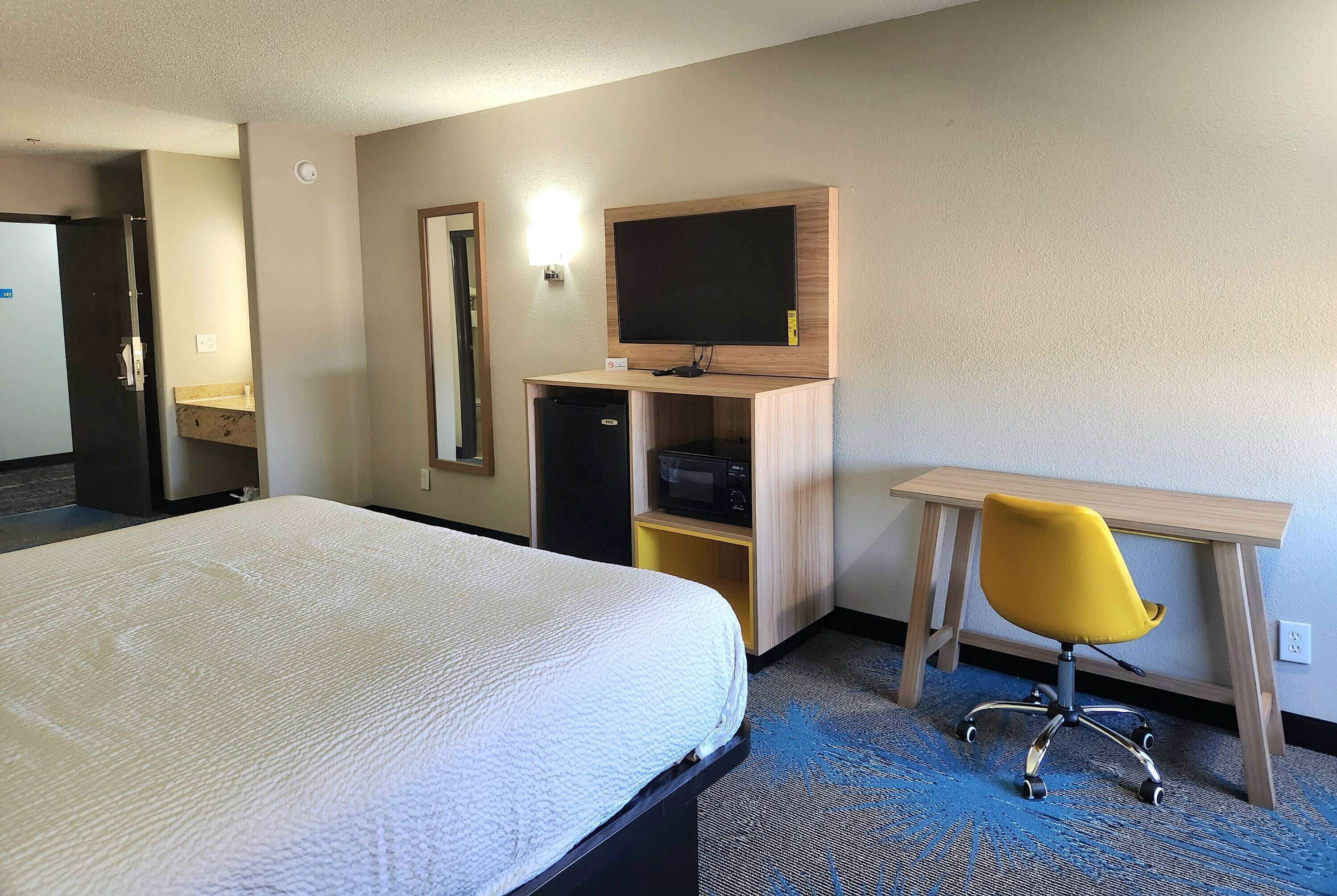 Ein Hotelzimmer mit einem Bett, einem Schreibtisch mit Stuhl, einem Fernseher und einer Mikrowelle.