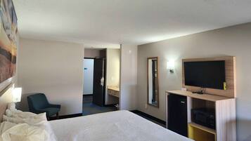 A hotel room with a large bed, a TV on a wooden stand, a desk with a computer, and a chair.