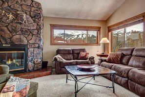 Cozy living room with a fireplace, large window, and mountain views.