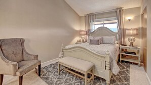 Une chambre à coucher comprenant un lit, une chaise, un banc, une table de chevet et une fenêtre avec des rideaux.