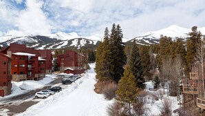 Une ville de montagne enneigée, avec des bâtiments rouges, une route recouverte de neige et des voitures garées.