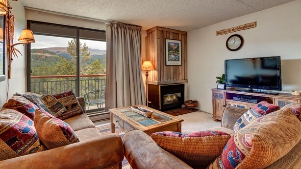 A cozy living room with a fireplace, a television, and a scenic view through the large window. - Trails End Condominiums by Great Western Lodging (Breckenridge)
