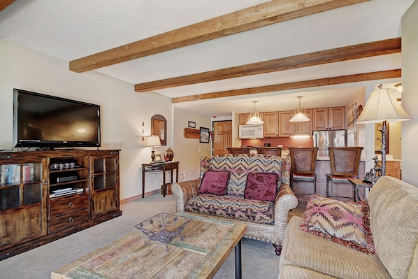 A living room with a television, wooden cabinet, patterned sofa, and a dining area with chairs and a table.