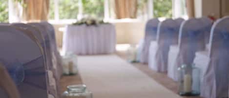 Rows of white chairs with blue sashes, arranged in a line with a carpeted aisle.