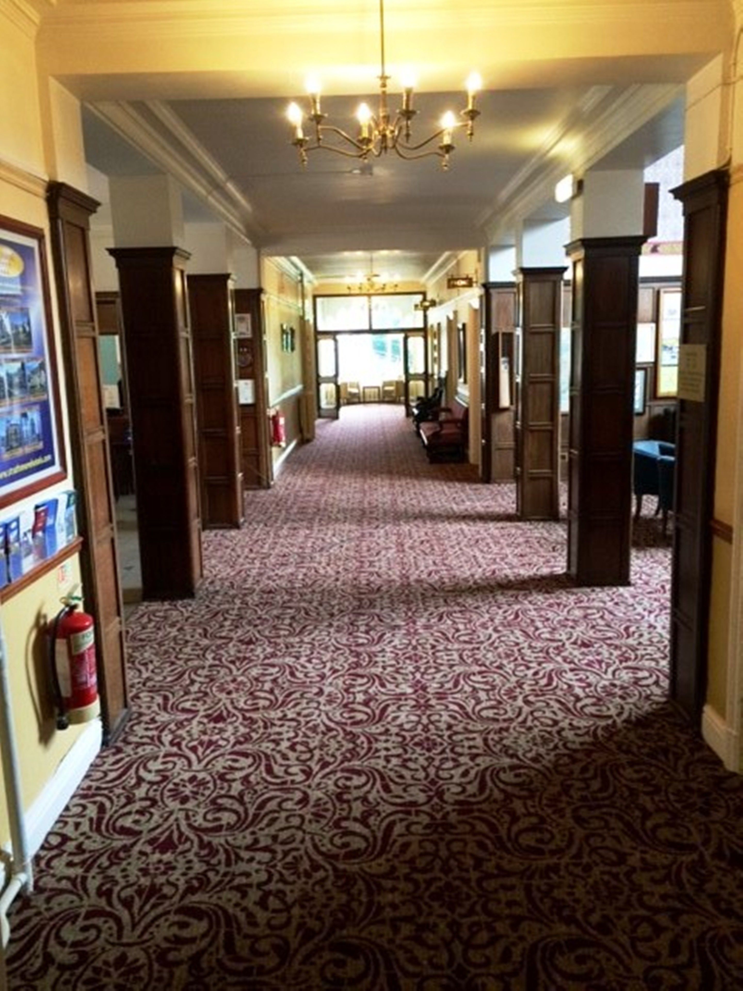 A hallway with patterned carpet, wooden doors, and a chandelier.