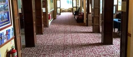 A hallway with patterned carpet, wooden doors, and a chandelier.
