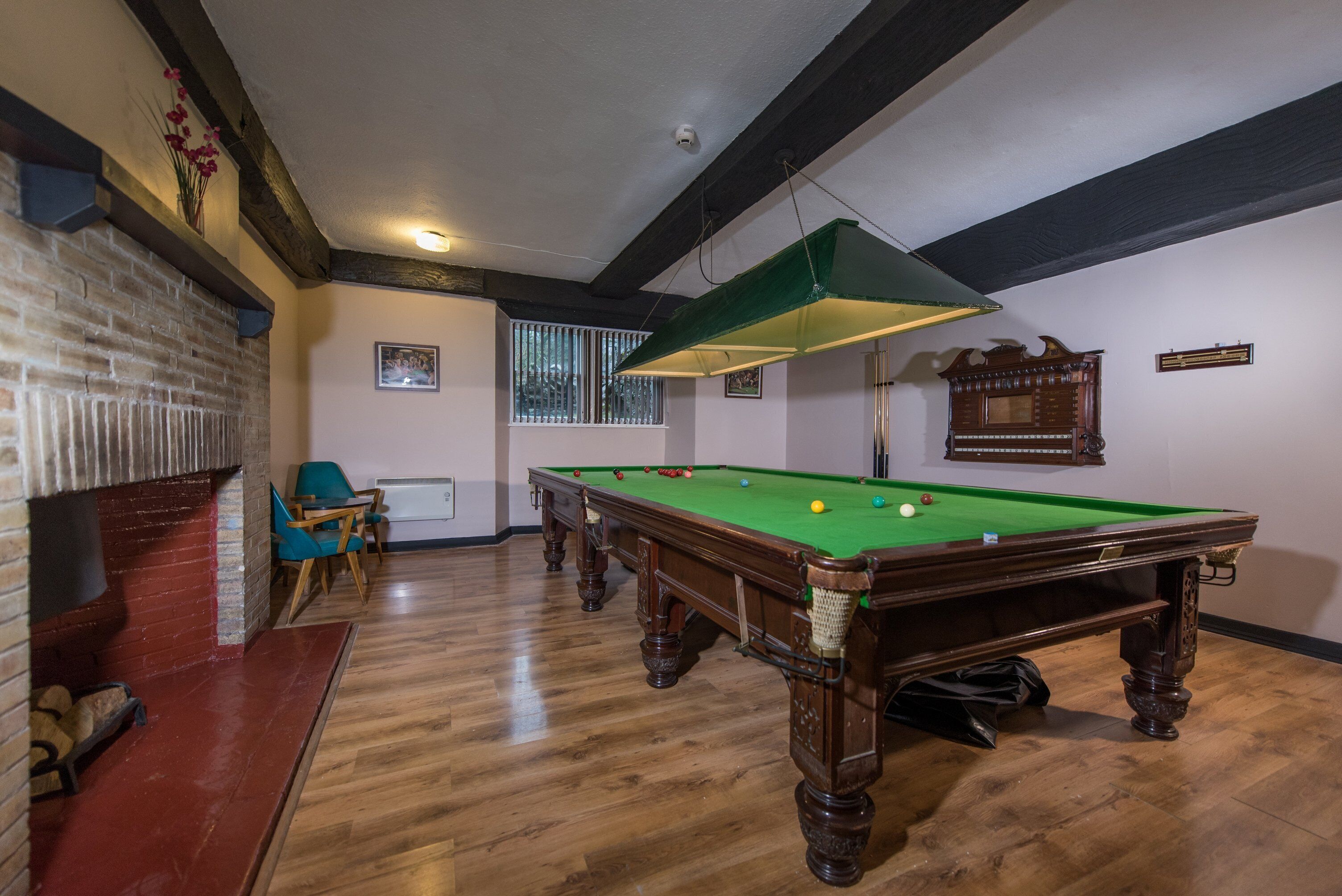 A billiards room with a pool table, chairs, and a fireplace.