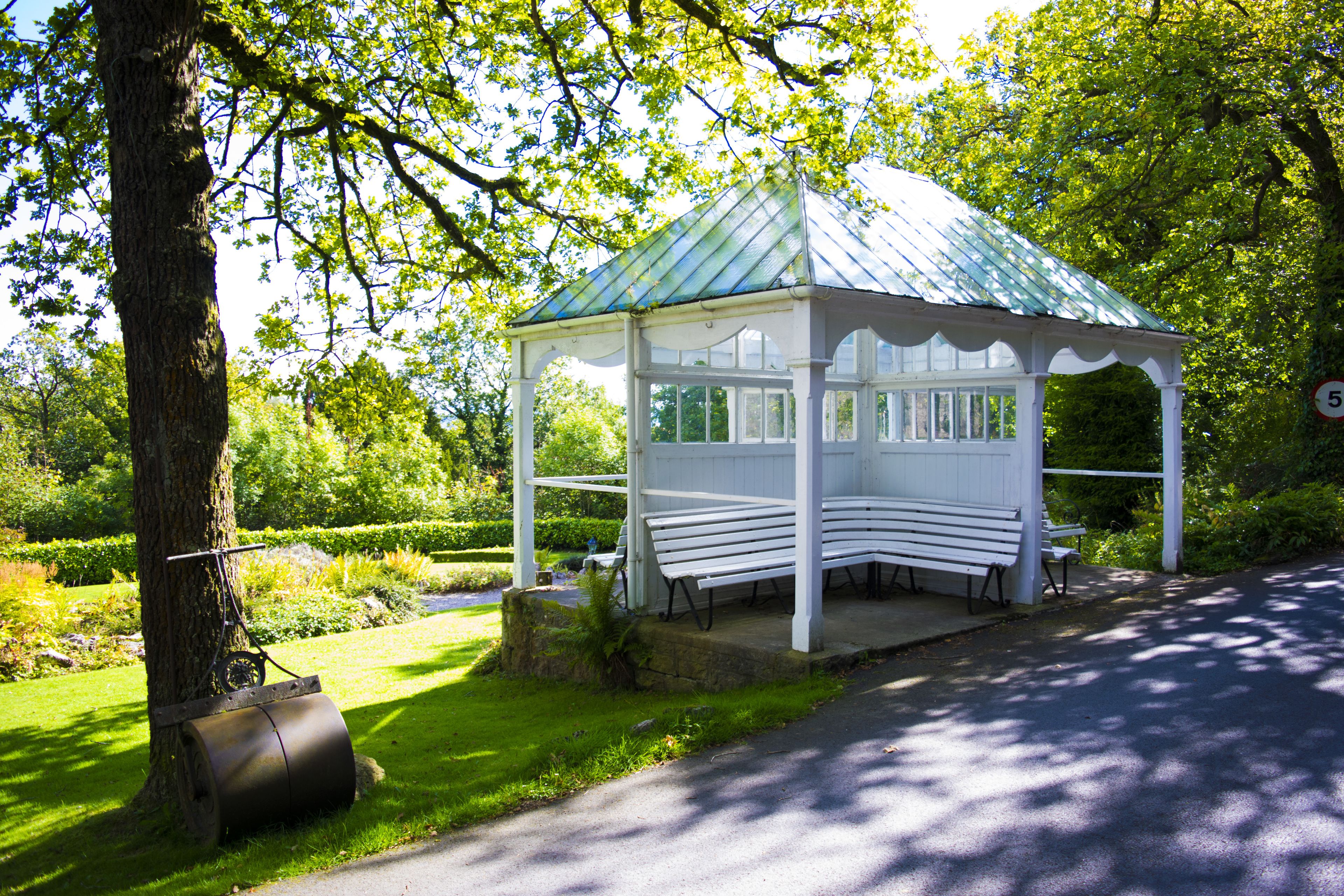 Ein Pavillon mit Bänken, umgeben von üppiger Vegetation und einem Baum.