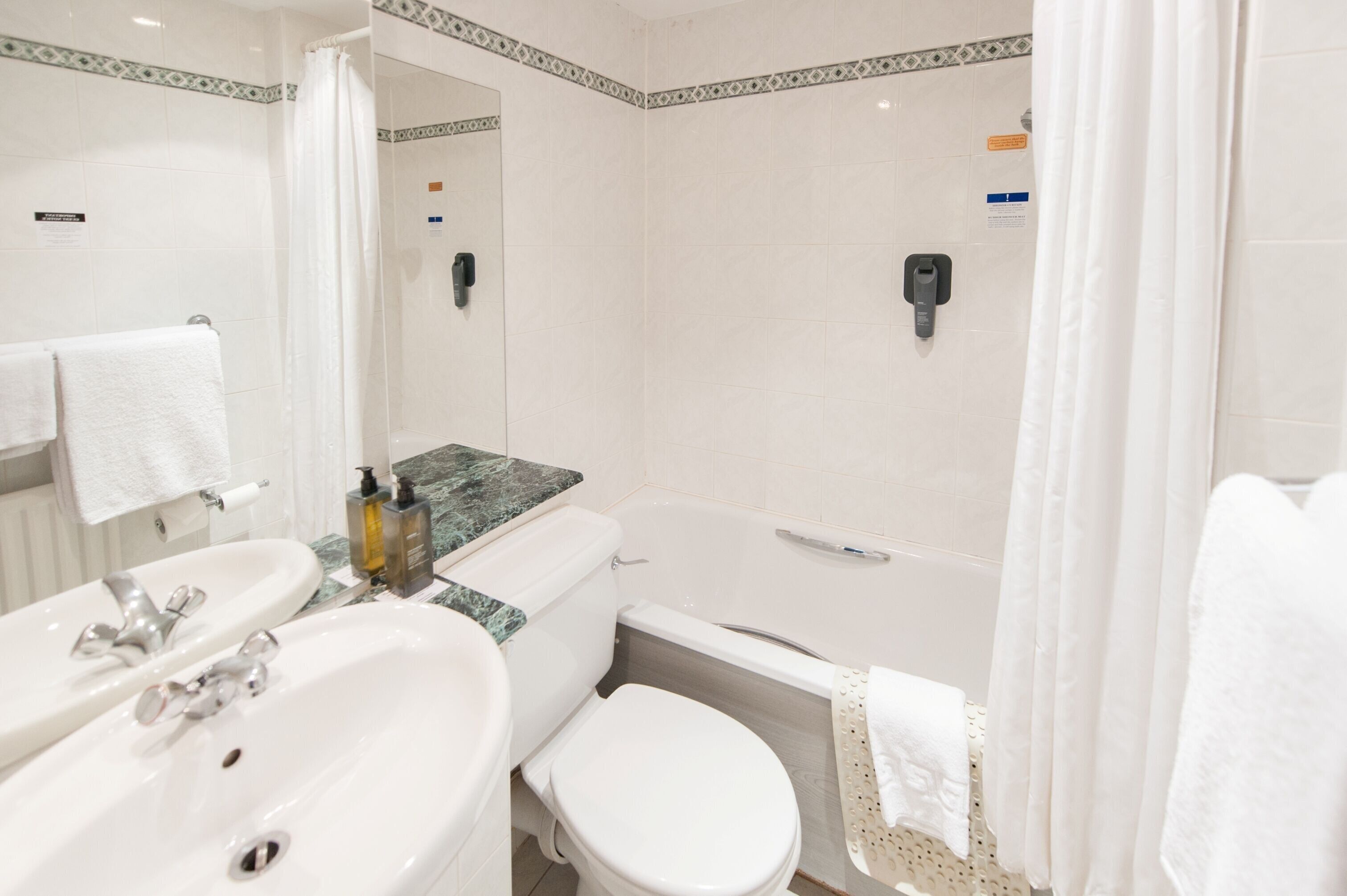 Un baño con lavamanos blanco, espejo, inodoro y zona de ducha.