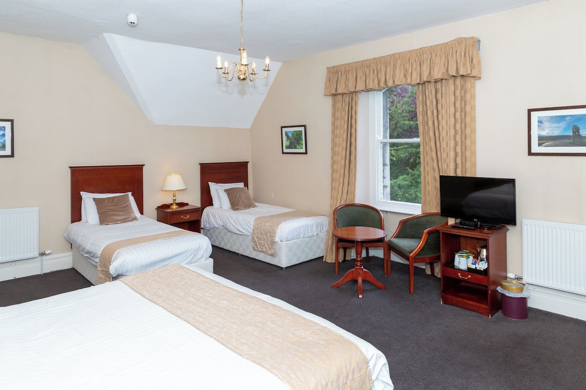 A hotel room with two beds, a television, a small table, and a window with curtains.