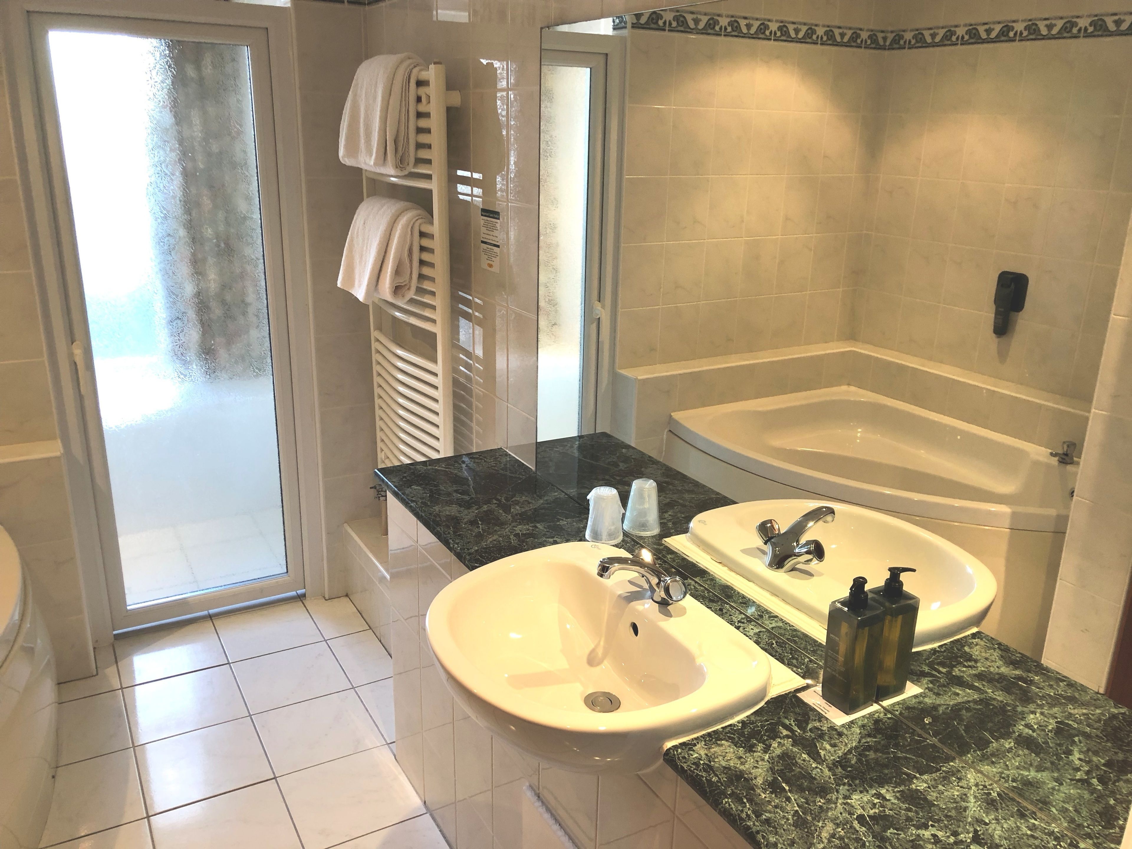 Un bagno con una vasca, due lavandini, un box doccia in vetro e un portascopino con asciugamani.
