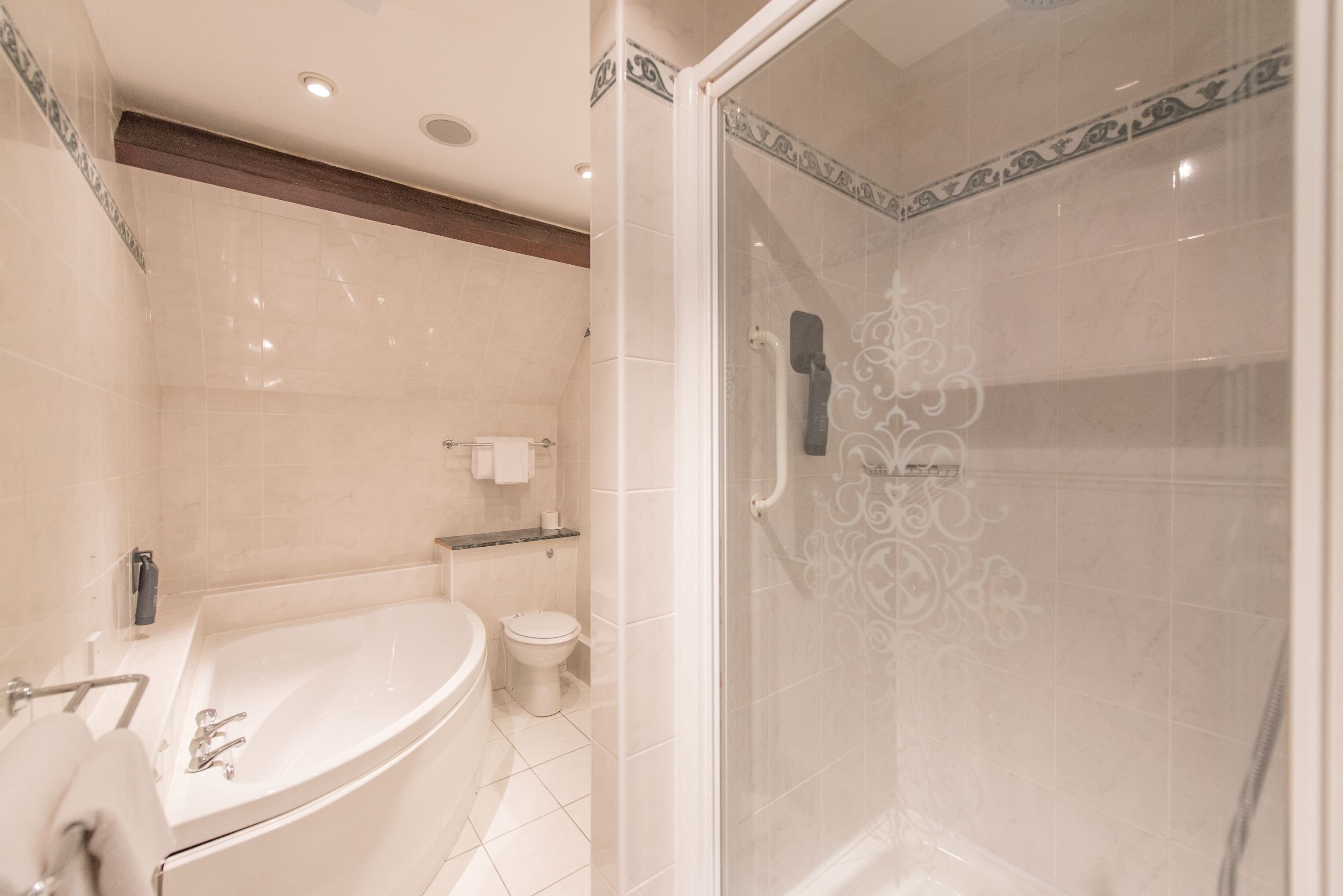 A modern bathroom with a bathtub, toilet, and glass-enclosed shower area.