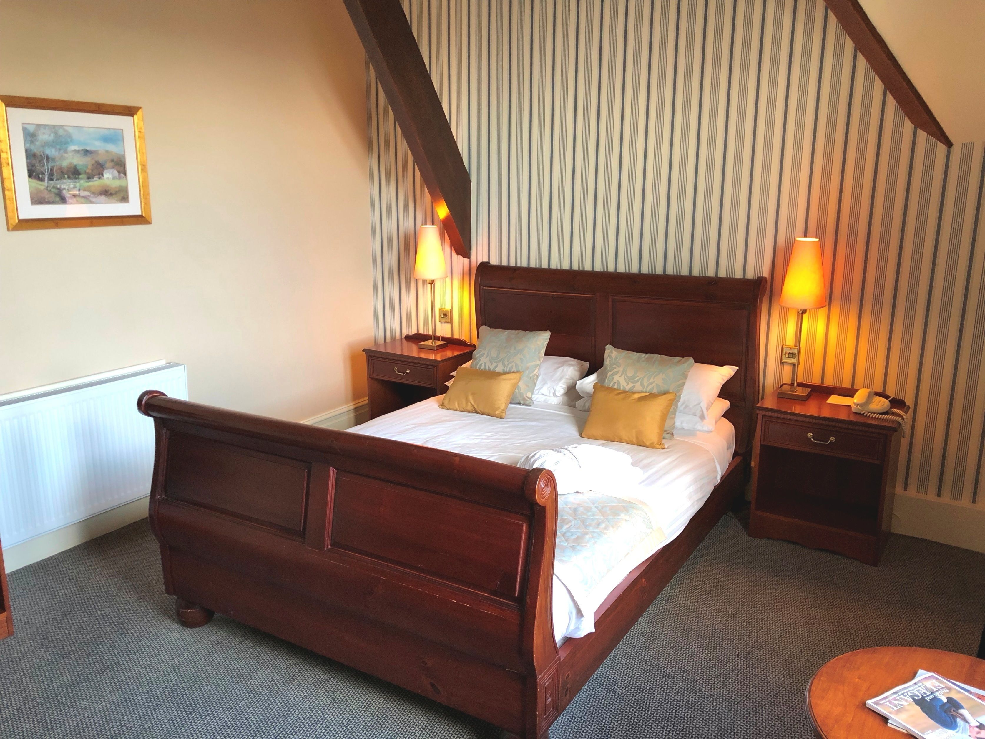 Una habitación de hotel ordenada con una cama grande, dos mesitas de noche y una pequeña mesa redonda.