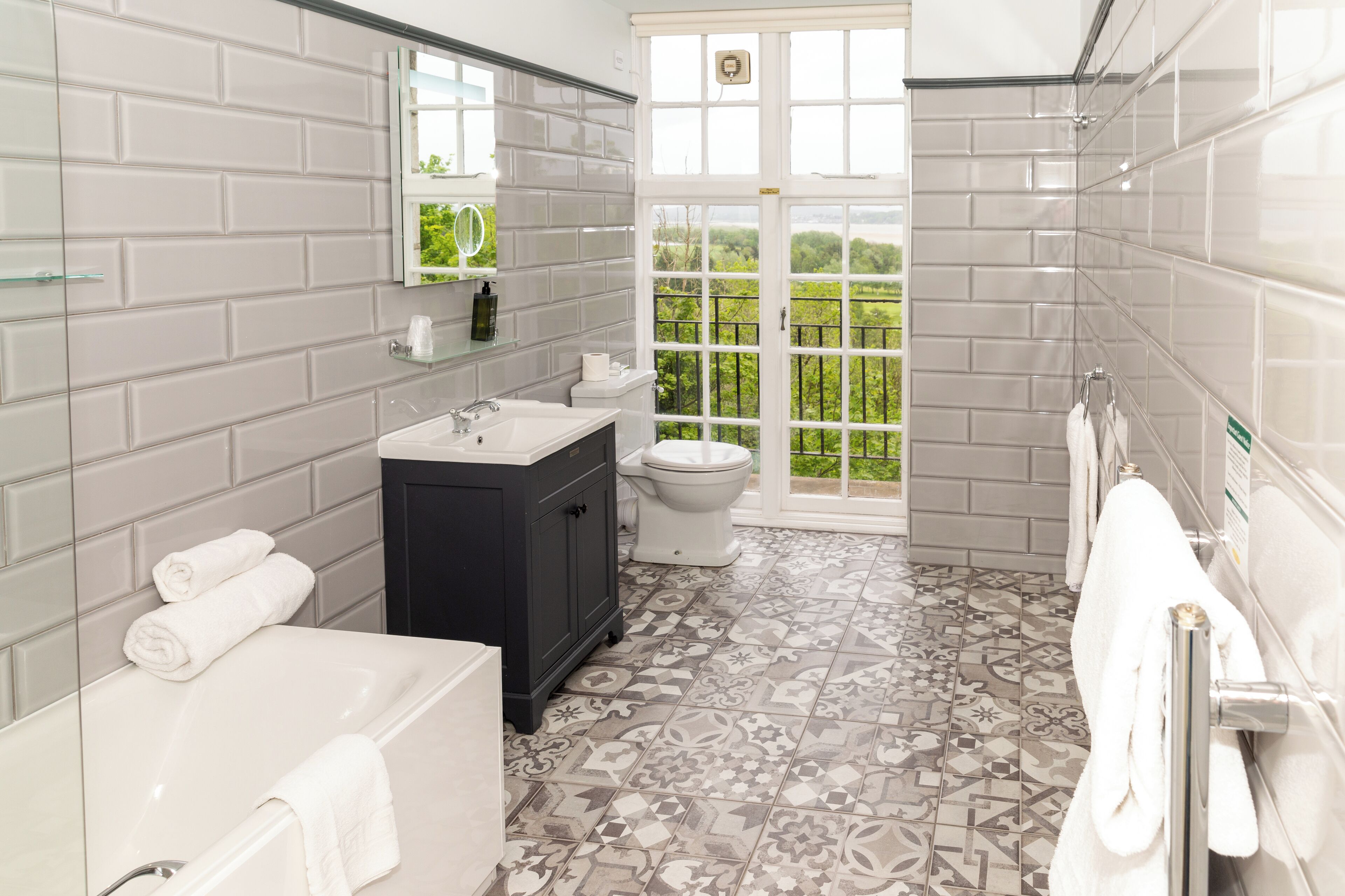 Un baño moderno con bañera, lavamanos e inodoro. Cuenta con un ventanal con vistas a zonas verdes y un balcón.