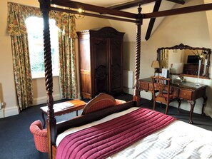 A four-poster bed with a red and white bedspread, a wooden desk with a mirror, and a large wardrobe in a room with floral curtains and a chandelier. - Cumbria Grand Hotel (Grange-over-Sands)