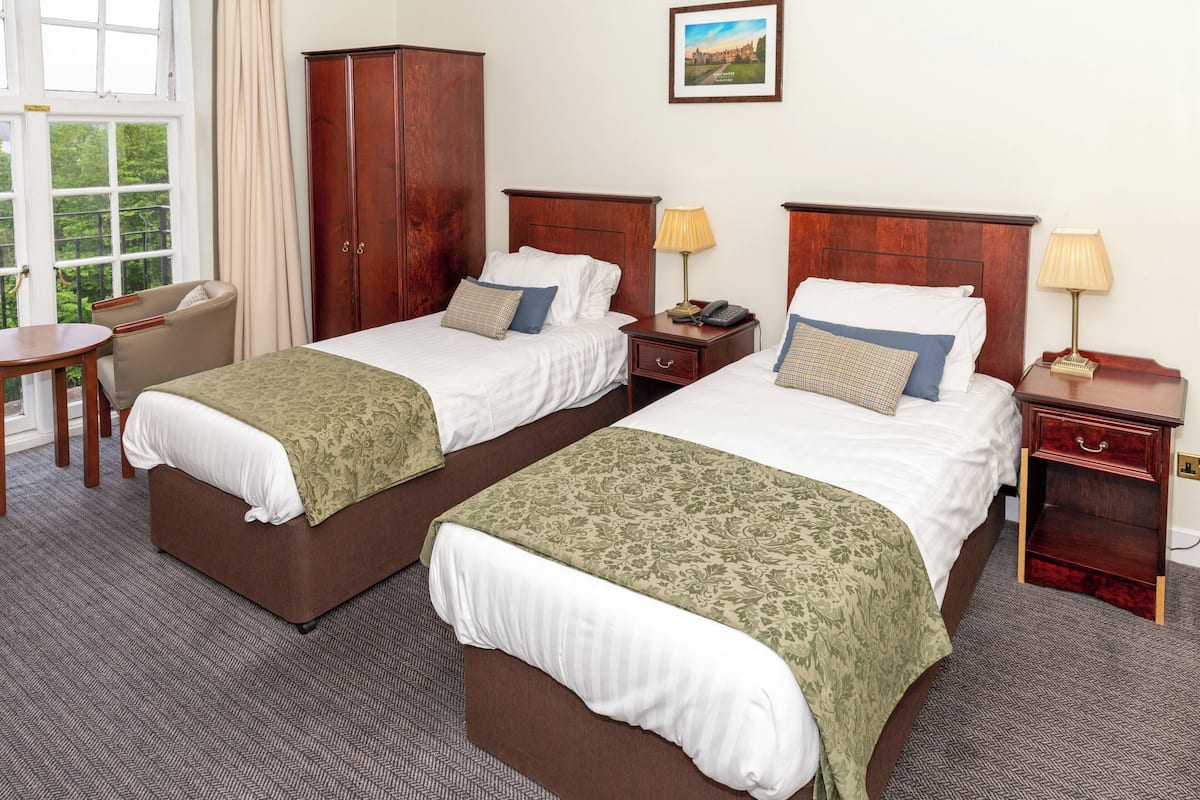 A hotel room with two beds, a wooden wardrobe, a desk, and a chair.